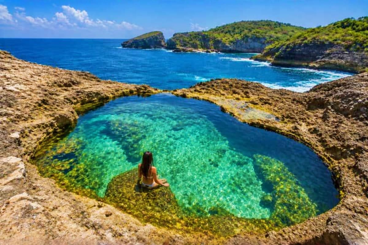 Arabian Honeymoon Escape to Indonesia Woman swimming in turquoise natural rock pool with limestone cliffs and blue ocean beyond in Indonesia