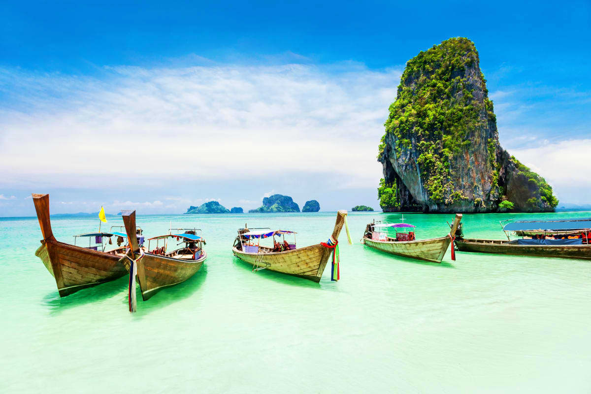 Traditional wooden longtail boats in turquoise waters near limestone cliff formations in Thailand