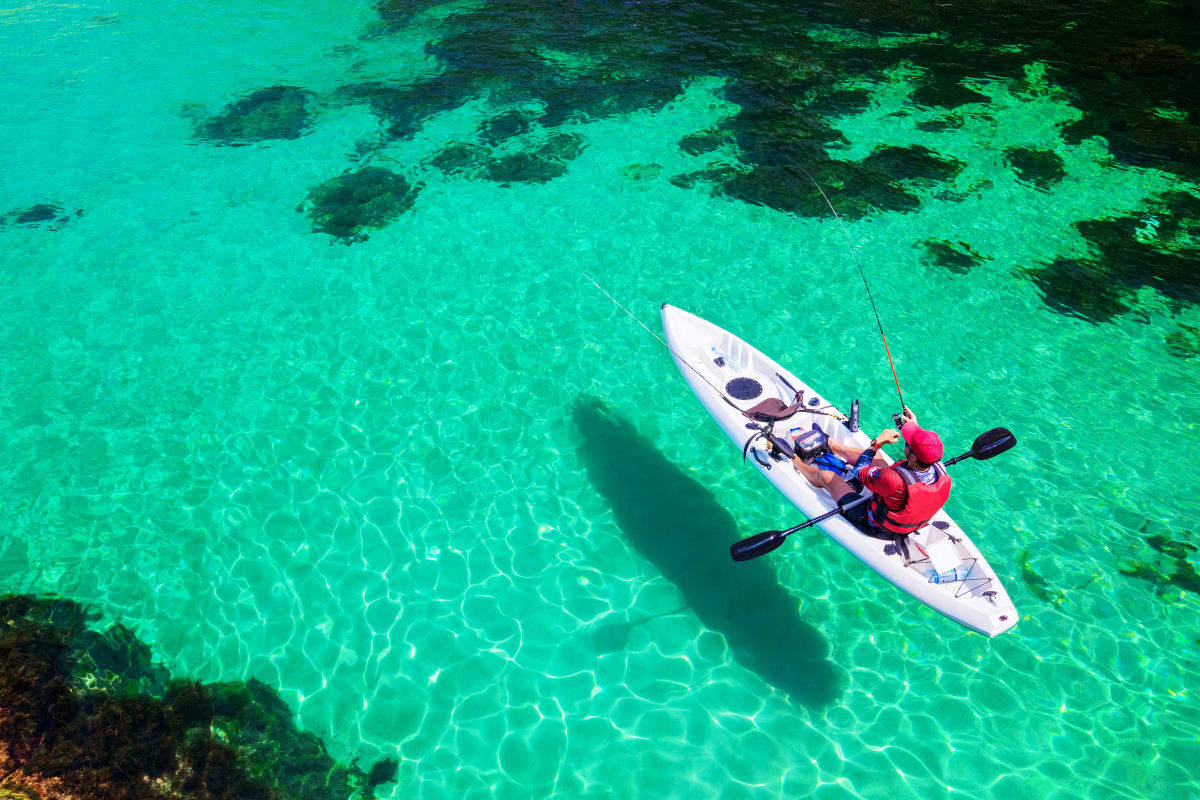 Phuket Krabi for All Ages Kayaker in red life jacket paddling white kayak in crystal clear turquoise water near rocky outcrops in tropical location