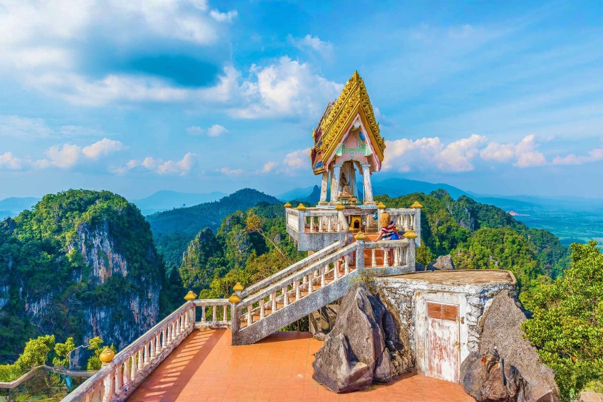 Buddhist temple with golden roof perched on mountainside cliff overlooking lush valleys and limestone peaks in Phuket, Thaila