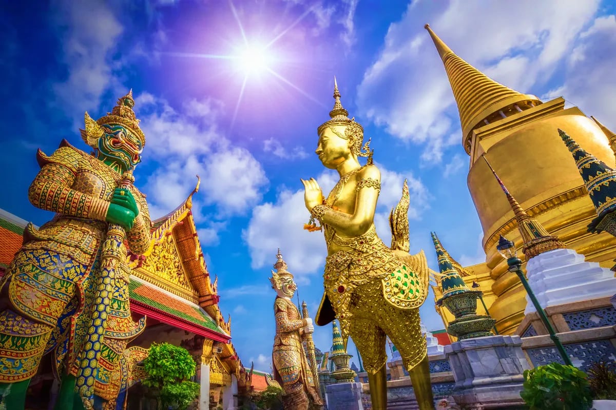 Golden Buddha statue and ornate temple spires with bright blue sky at a Buddhist temple in Bangkok, Thailand