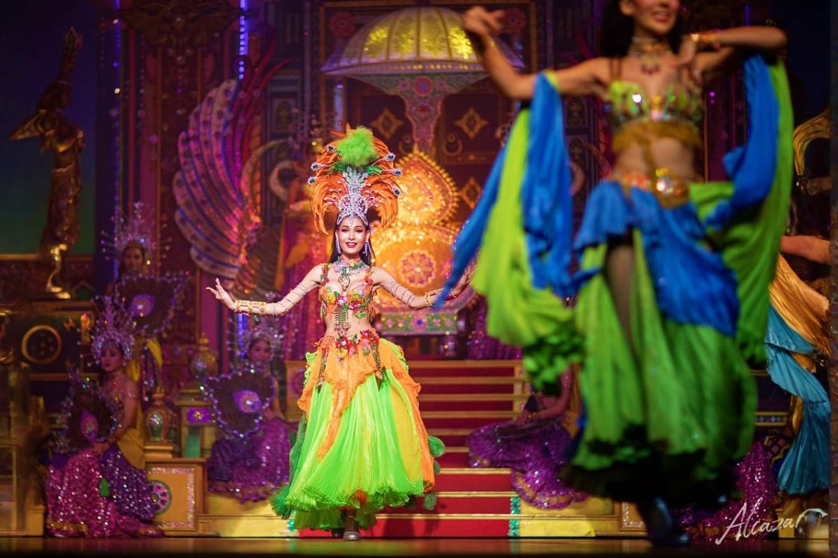 Cabaret performer in ornate golden headdress and green costume dancing on stage in Bangkok theater production.