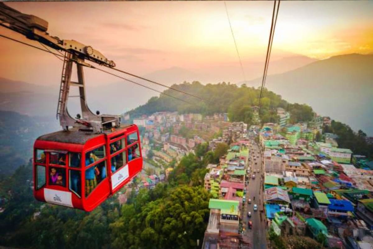 Red cable car suspended over Shimla hillside town with colorful buildings and forested mountains at sunset