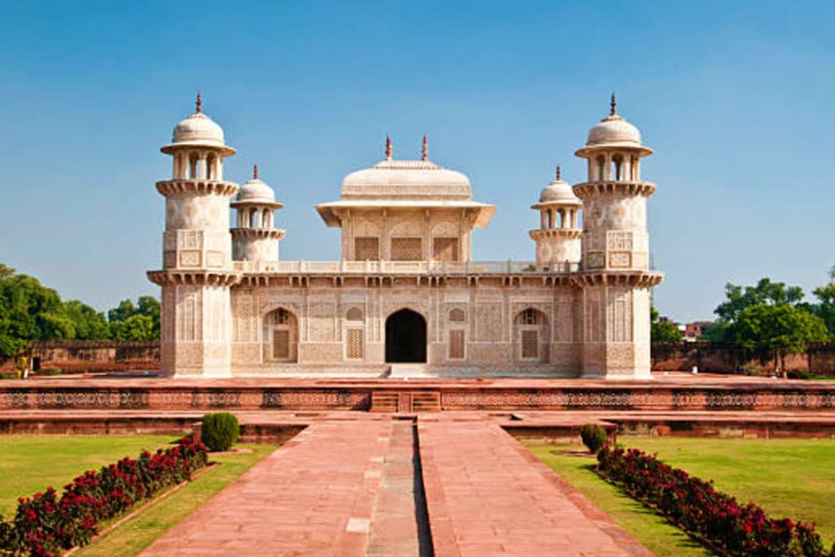 White marble Mughal mausoleum with domed towers and symmetrical architecture, red brick pathway with manicured gardens in for