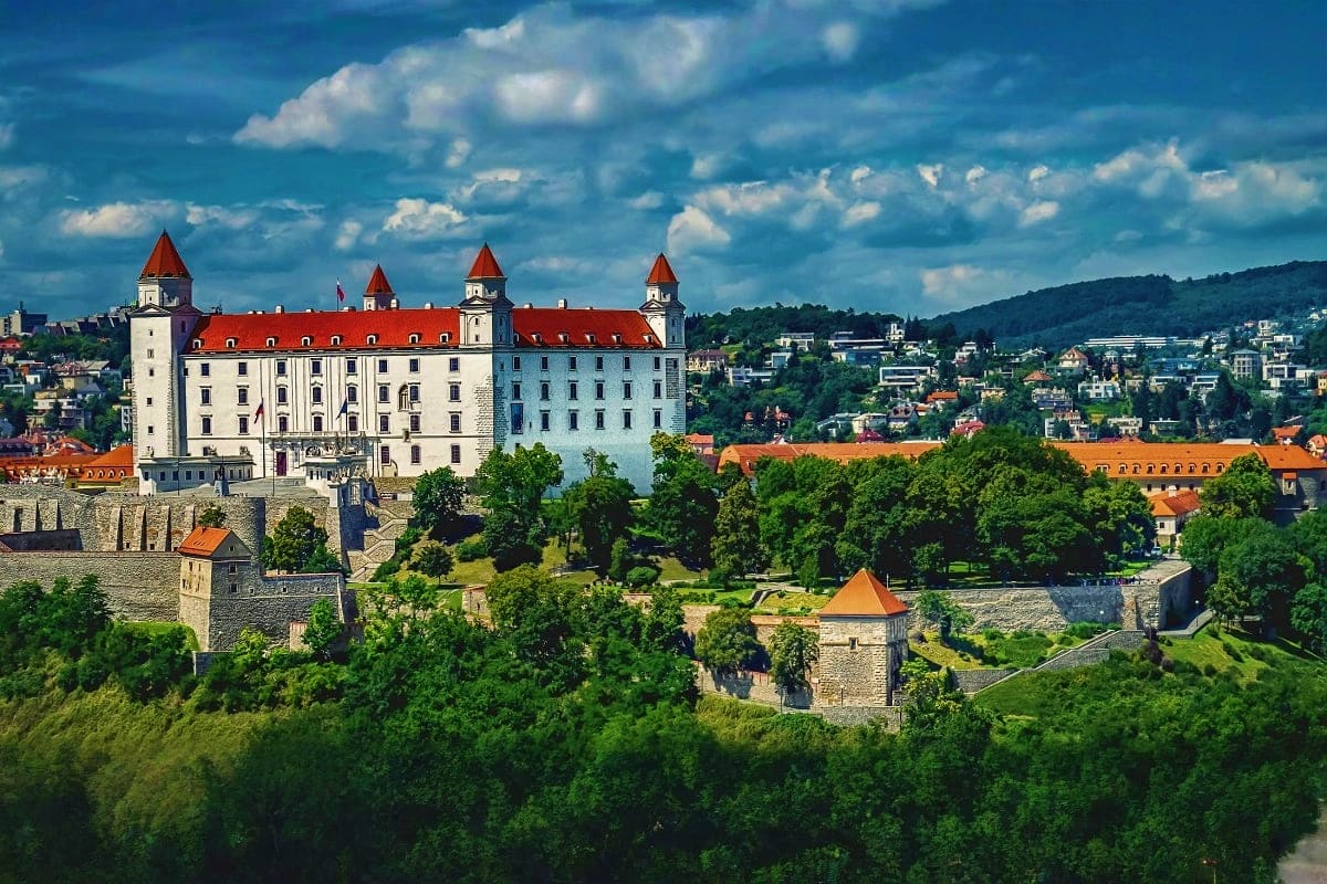 Bratislava Castle with red-tiled roofs and white stone walls overlooking the Danube River and forested valley in Slovakia