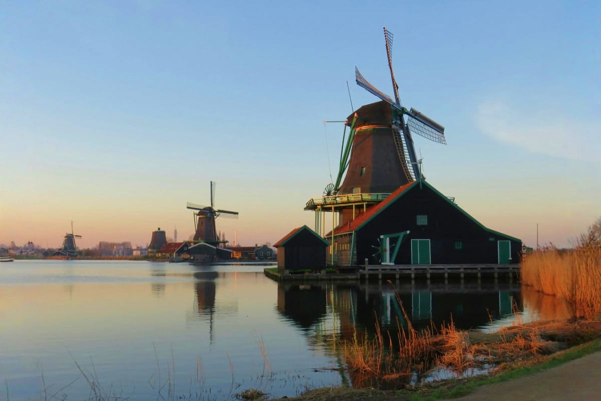 Traditional Dutch windmills reflected in still water at sunset in Zaanse Schans, Netherlands