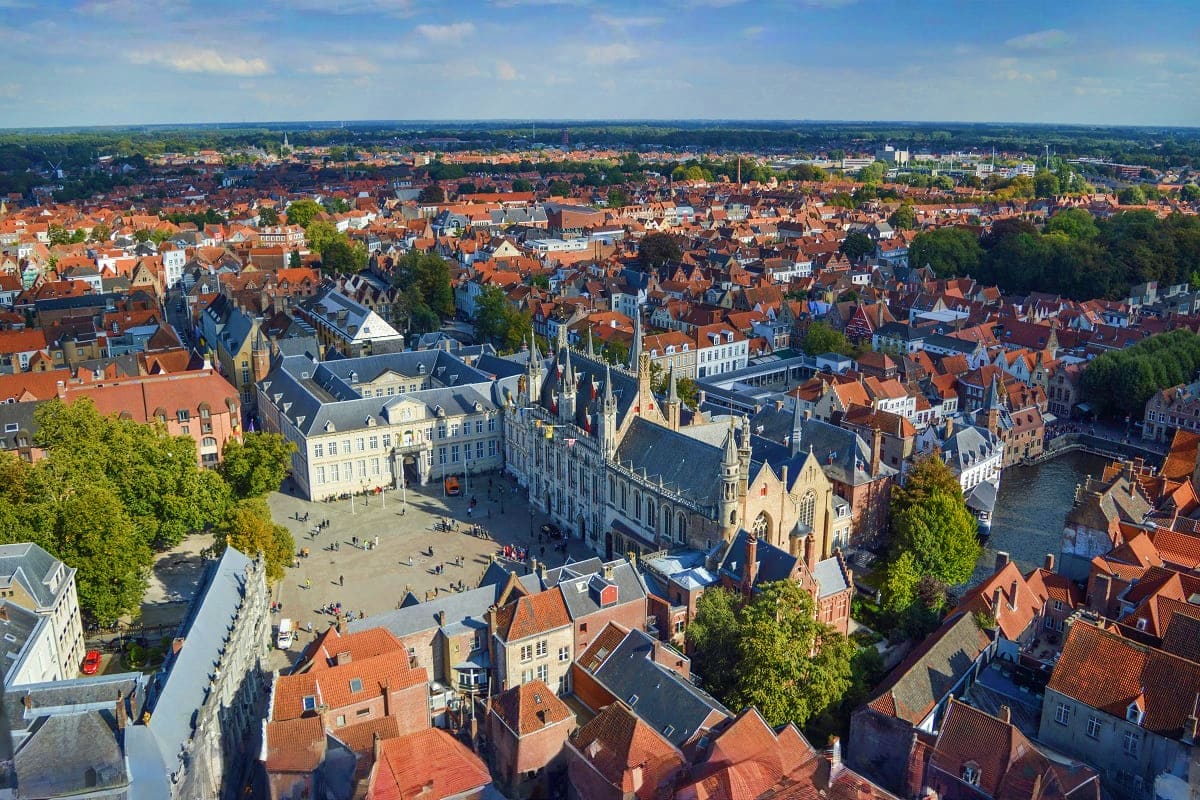 Aerial view of a historic European city with red-roofed buildings, a Gothic church, and town square surrounded by medieval ar