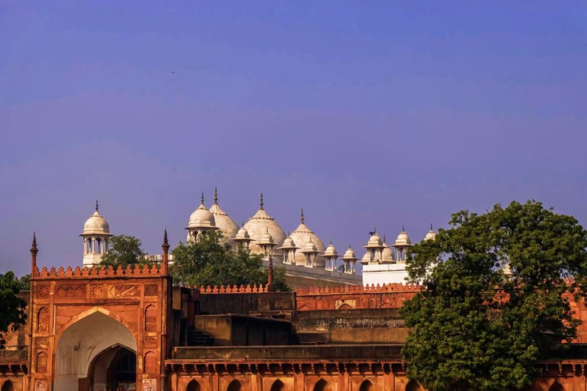 Red sandstone fort with white domed structures and golden spires against blue sky, Delhi landmark for Golden Triangle tour
