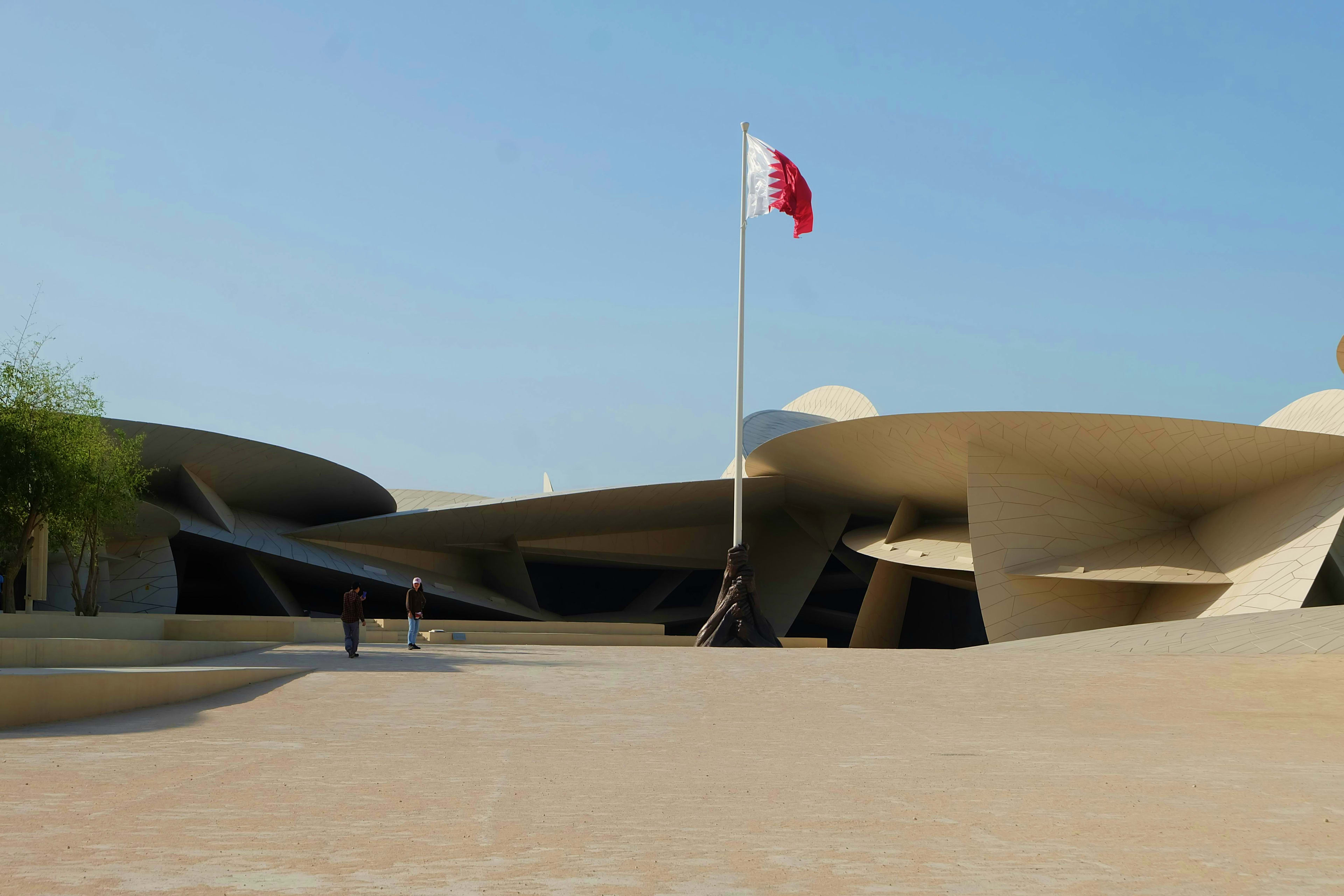 Qatar flag flying above modern architectural building with curved concrete design in desert plaza