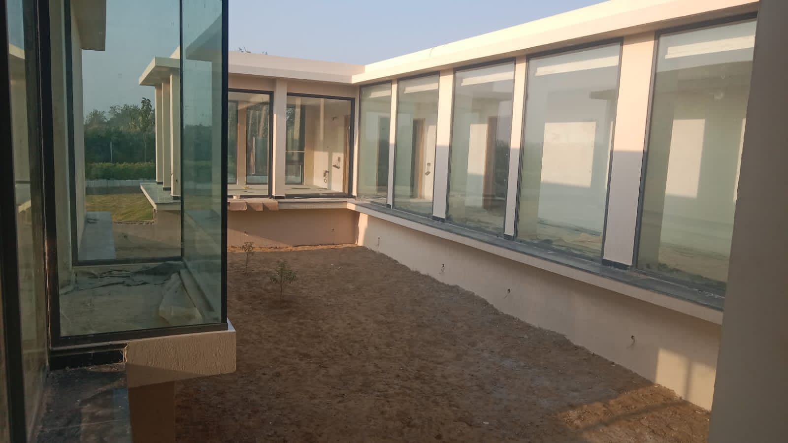 Farmhouse corridors with glass walls connecting interior spaces to landscaped outdoors, showcasing modern residential architecture in Noida.