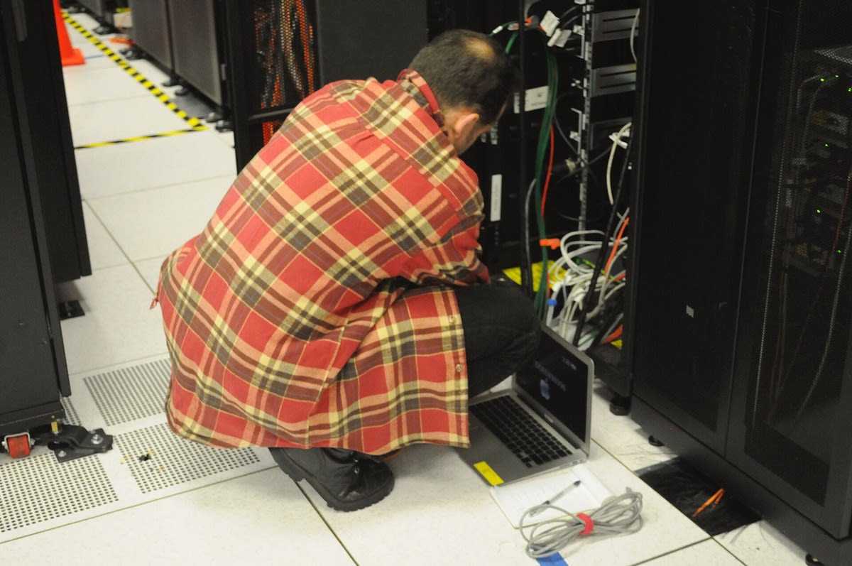 Photo of a technician with a laptop working on a server rack in a data center
