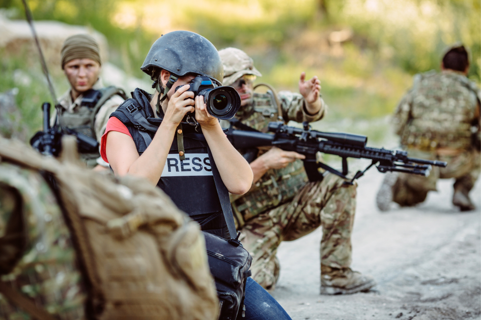 Journalist filming with a camera crew while wearing a press vest in a conflict zone