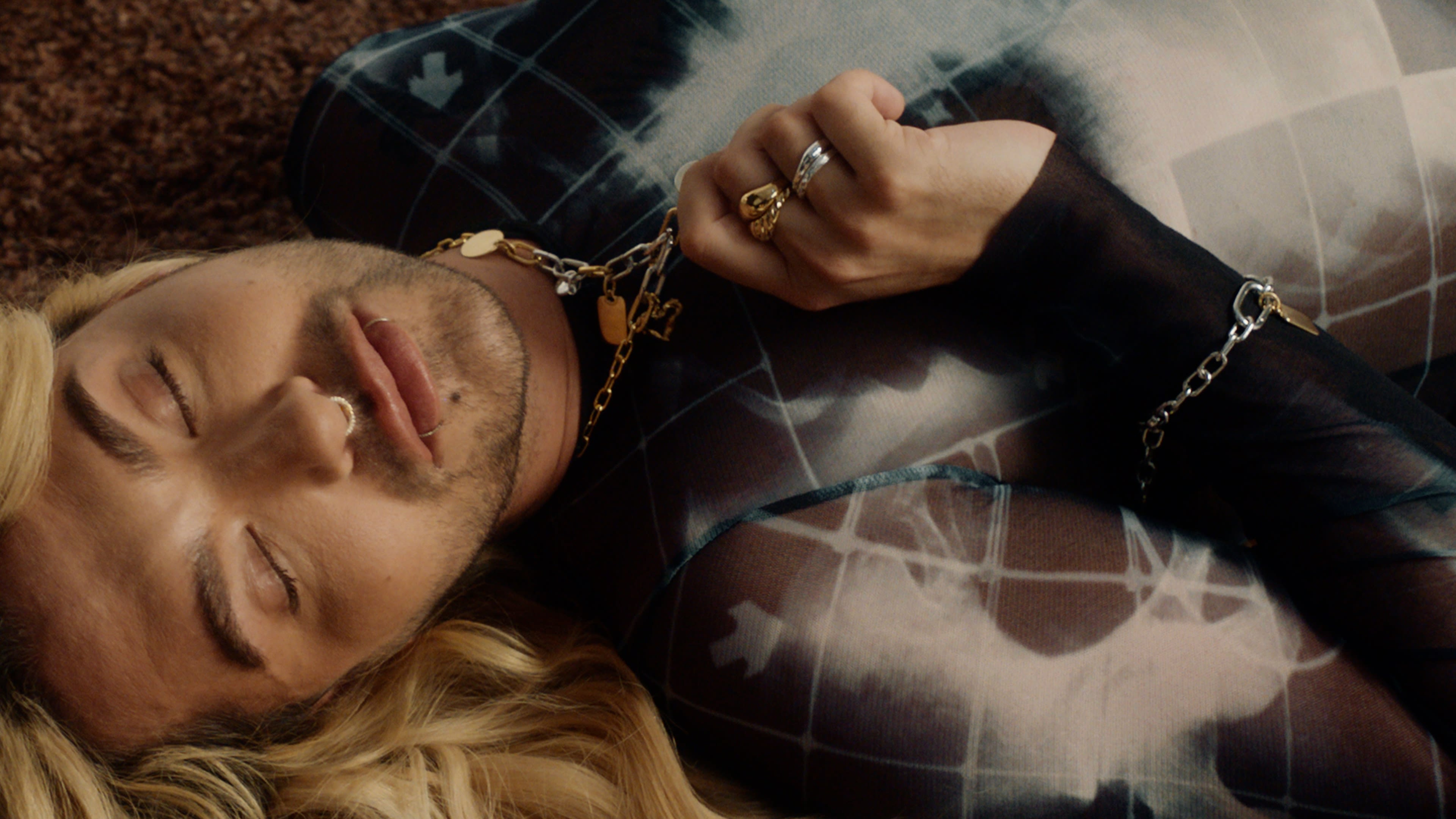 Stilvolles Porträt eines Mannes mit blonden Haaren und Schmuck; warme Farbkorrektur betont Atmosphäre.