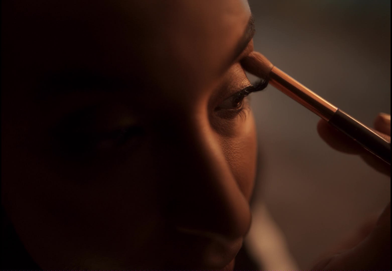 Warm color-grading: Detail shot einer Person beim Make-up, emotionaler Blick.