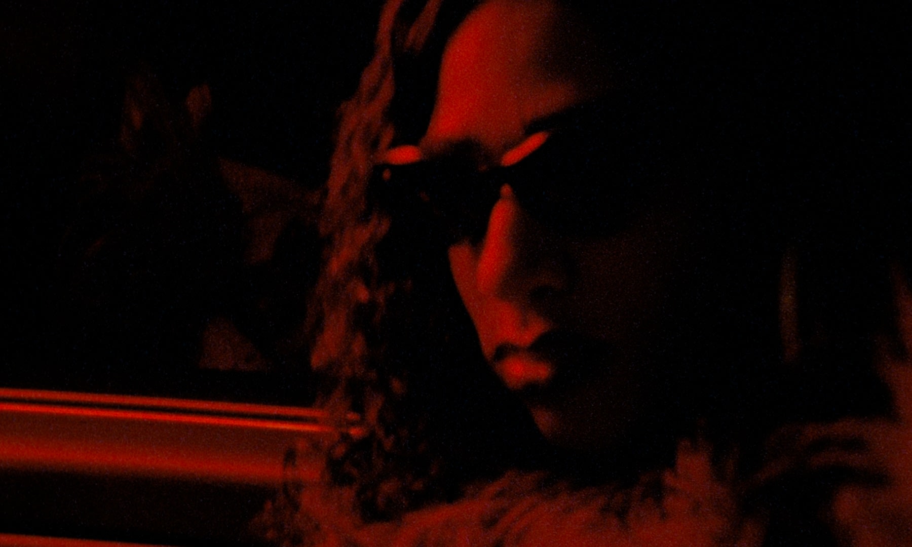 Dramatisches rotes Grading: Frau mit Sonnenbrille in geheimnisvoller, kontrastreicher Nachtstimmung.