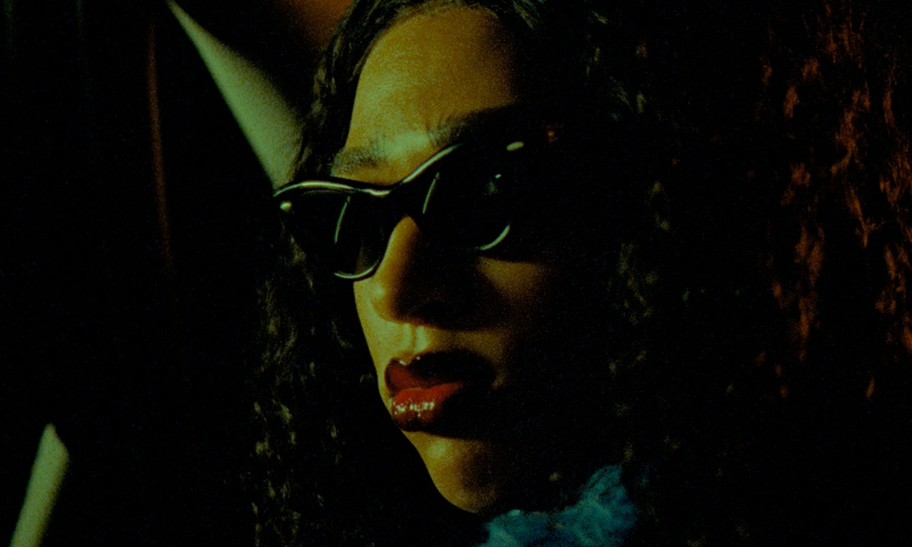 Mystisches Porträt mit Sonnenbrille, intensives color-grading, gelb-orange Haut, rote Lippen.