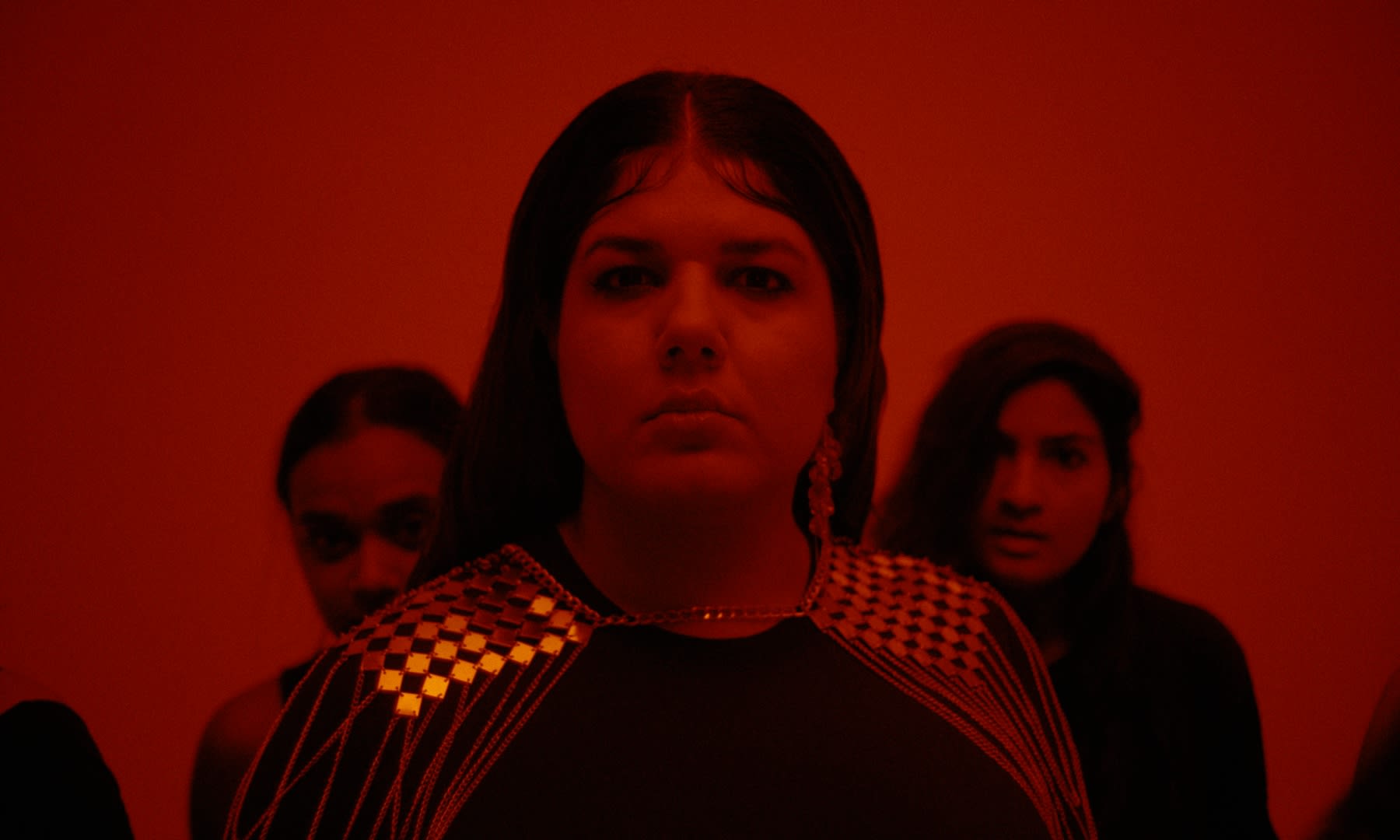 Intensives rotes Color-Grading unterstreicht die ernste Stimmung der Frau mit Goldschmuck.