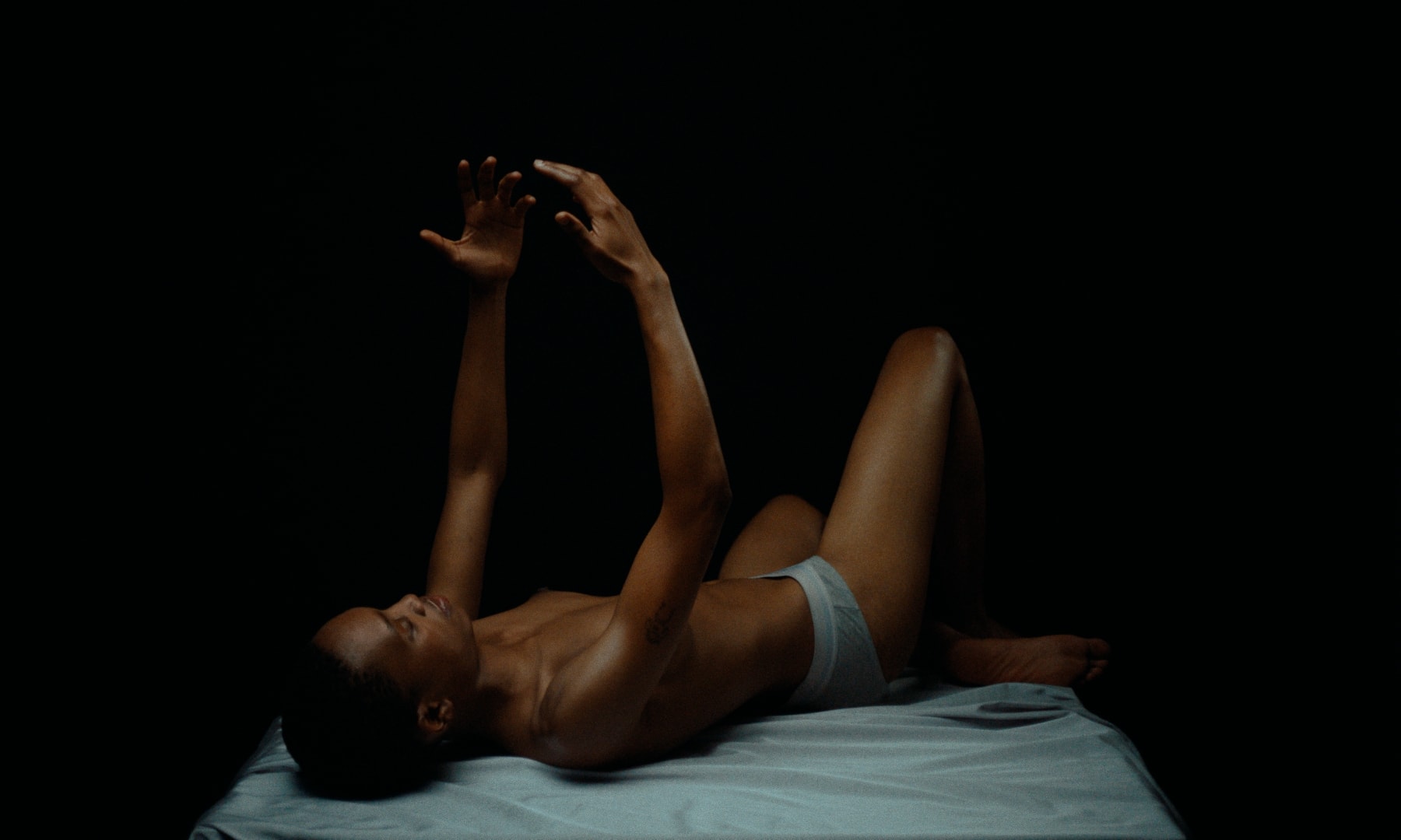 Dramatisches color-grading betont warme Hauttöne und kühle Stofftexturen in dunkler Umgebung.