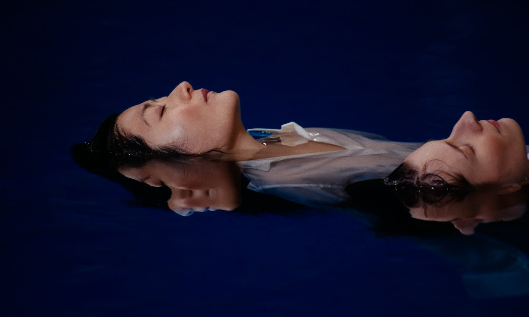 Zwei Frauen schweben im dunklen Blau, die Schönheit durch präzises Color-Grading betont.