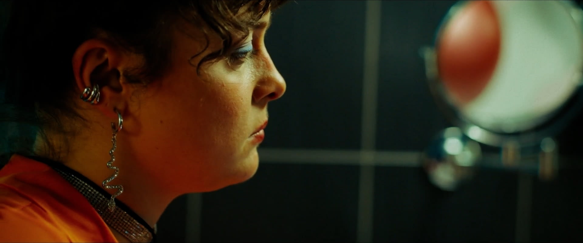 Colorist-Nahaufnahme mit intensiver Farbkorrektur, warmer Beleuchtung und auffälligem Schmuck.