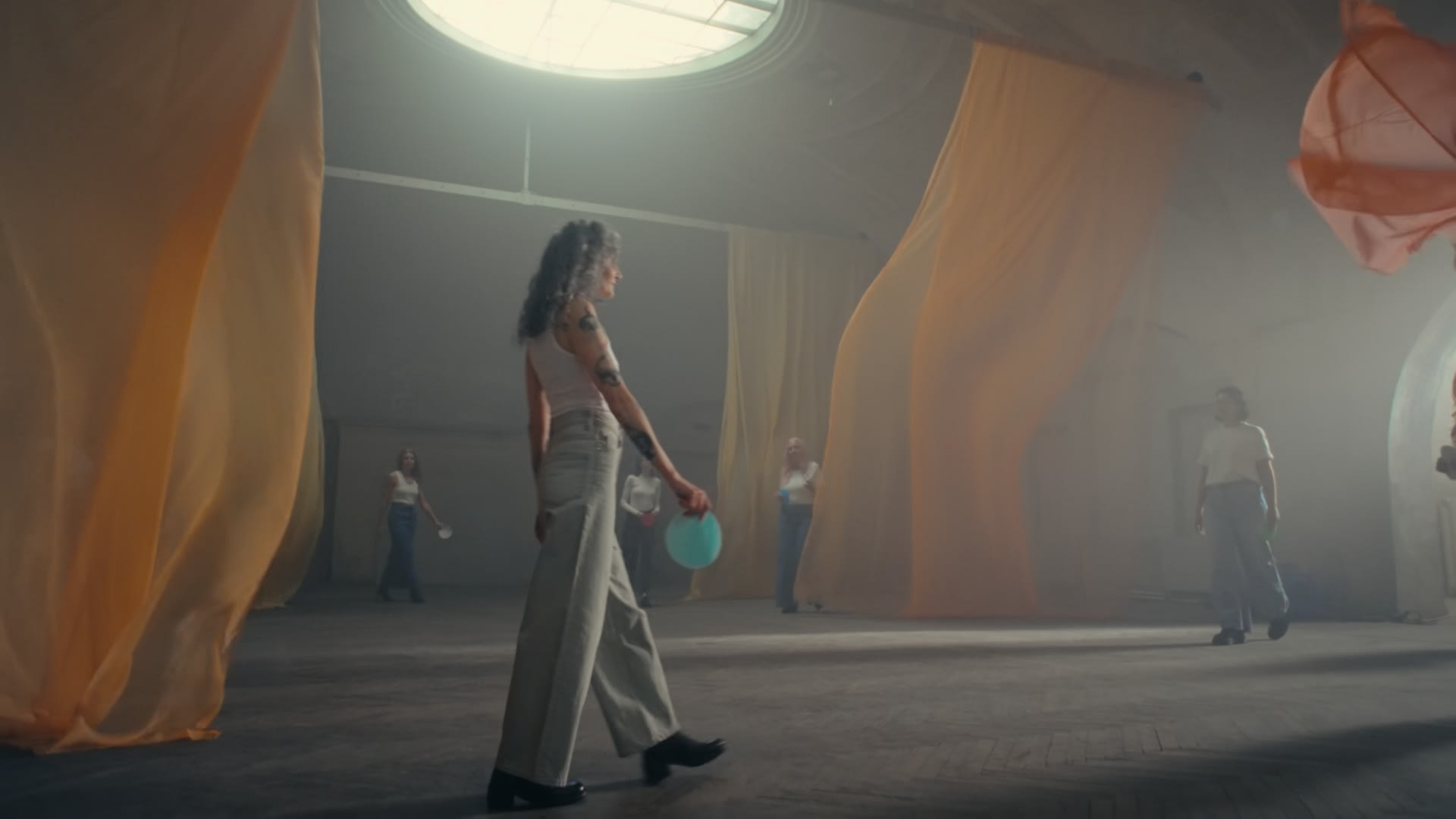 Rauchige Halle, orangefarbene Stoffe und Frau mit Ballon; stimmungsvolles Color-Grading.