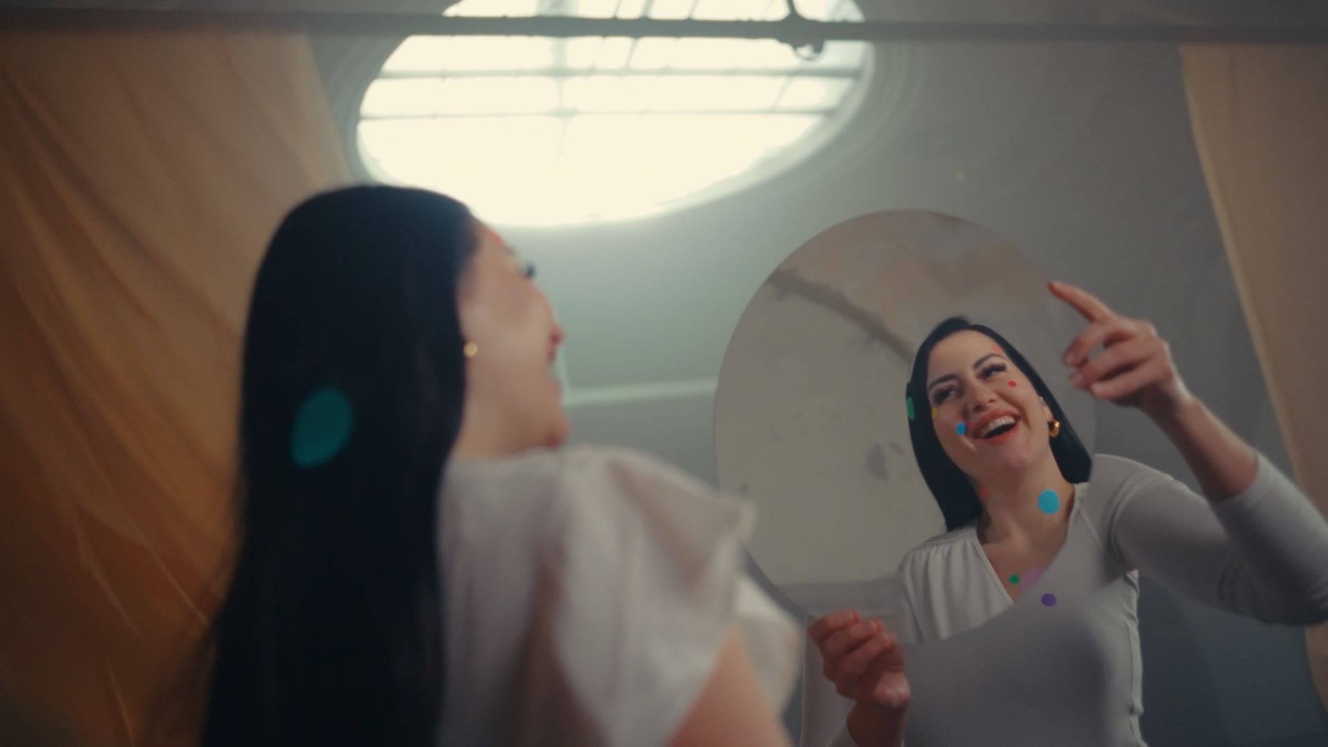 Lachende Frau mit bunten Konfetti-Punkten im Spiegel. Unser Color-Grading betont pure Lebensfreude.