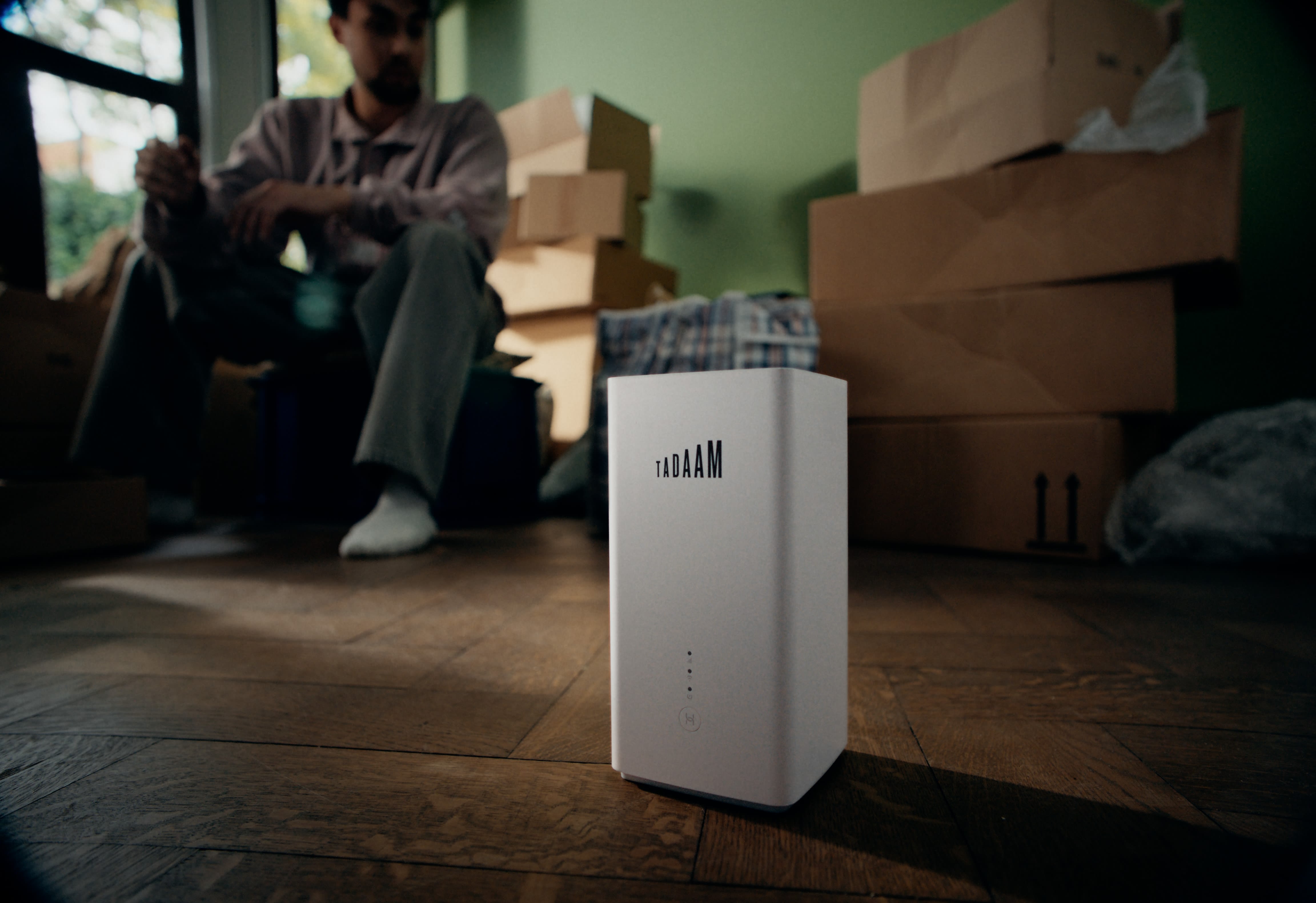 Natürliches colour-grading einer Umzugsszene: Mann und TADAAM Modem auf Holzboden.