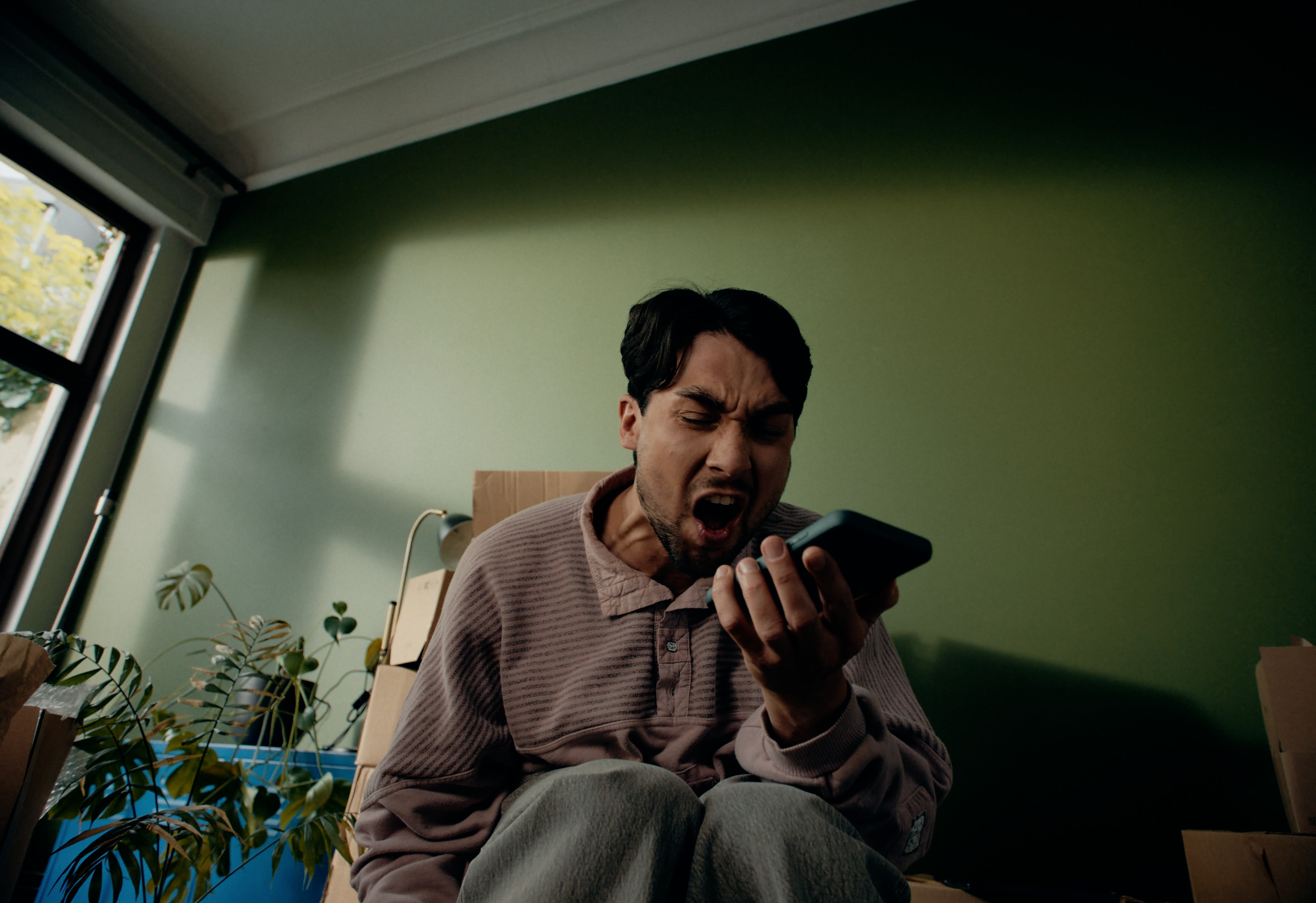 Farbkorrektur betont die Wut eines Mannes, der ins Handy schreit, in gedämpft grünem Raum.