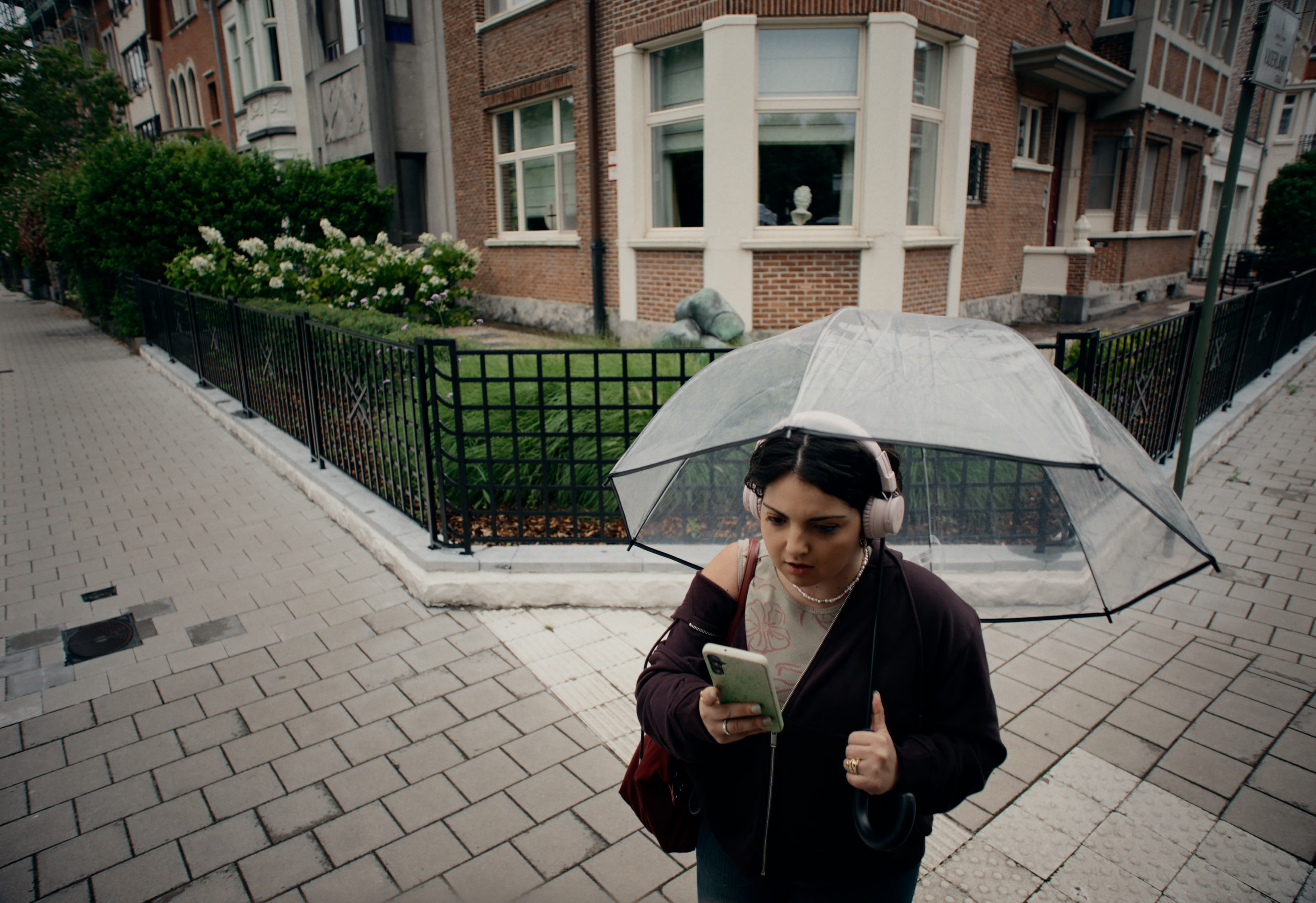 Frau mit Regenschirm prüft Handy, natürliches Color-Grading für eine ruhige Stadtszene.
