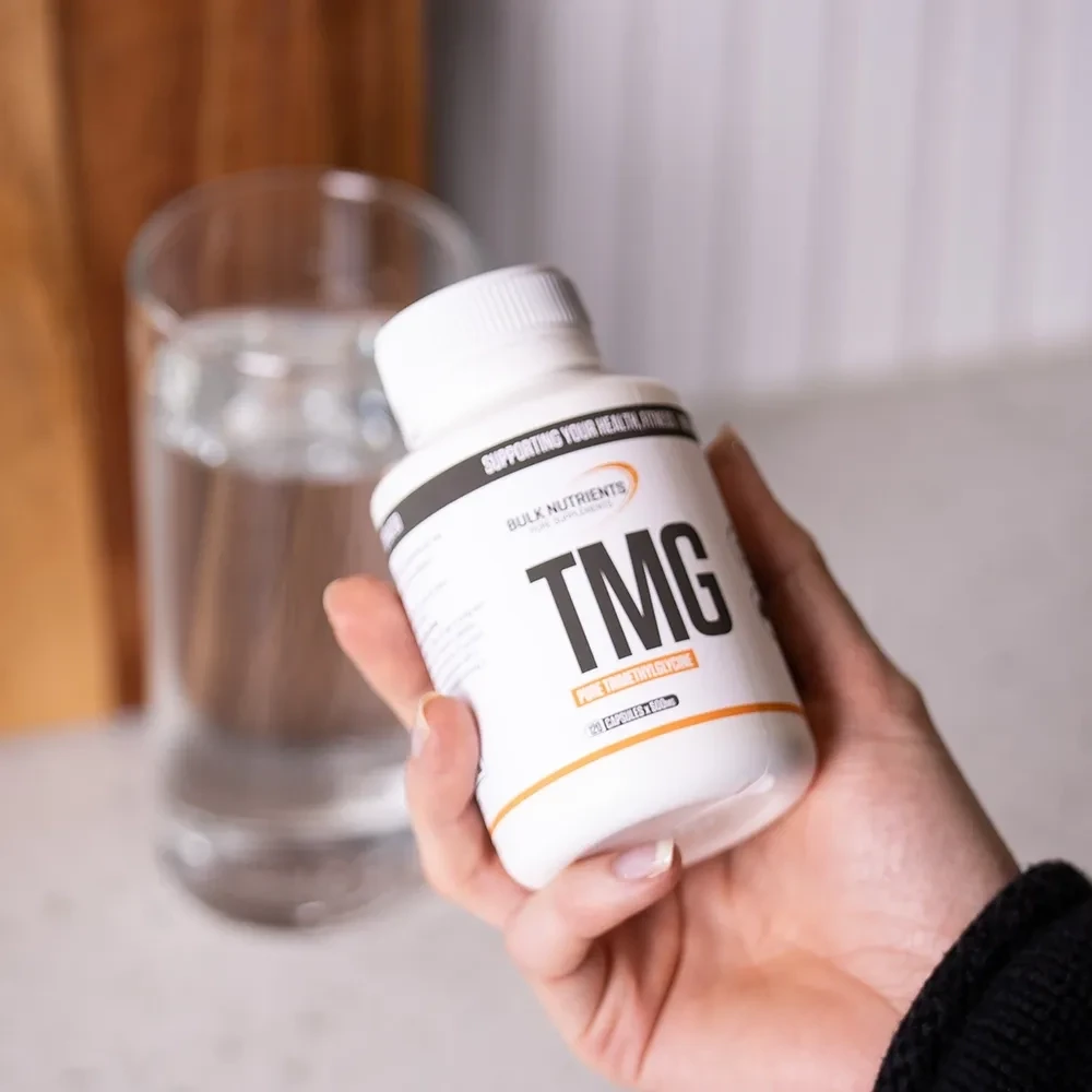 TMG Capsules being held right hand with glass of water