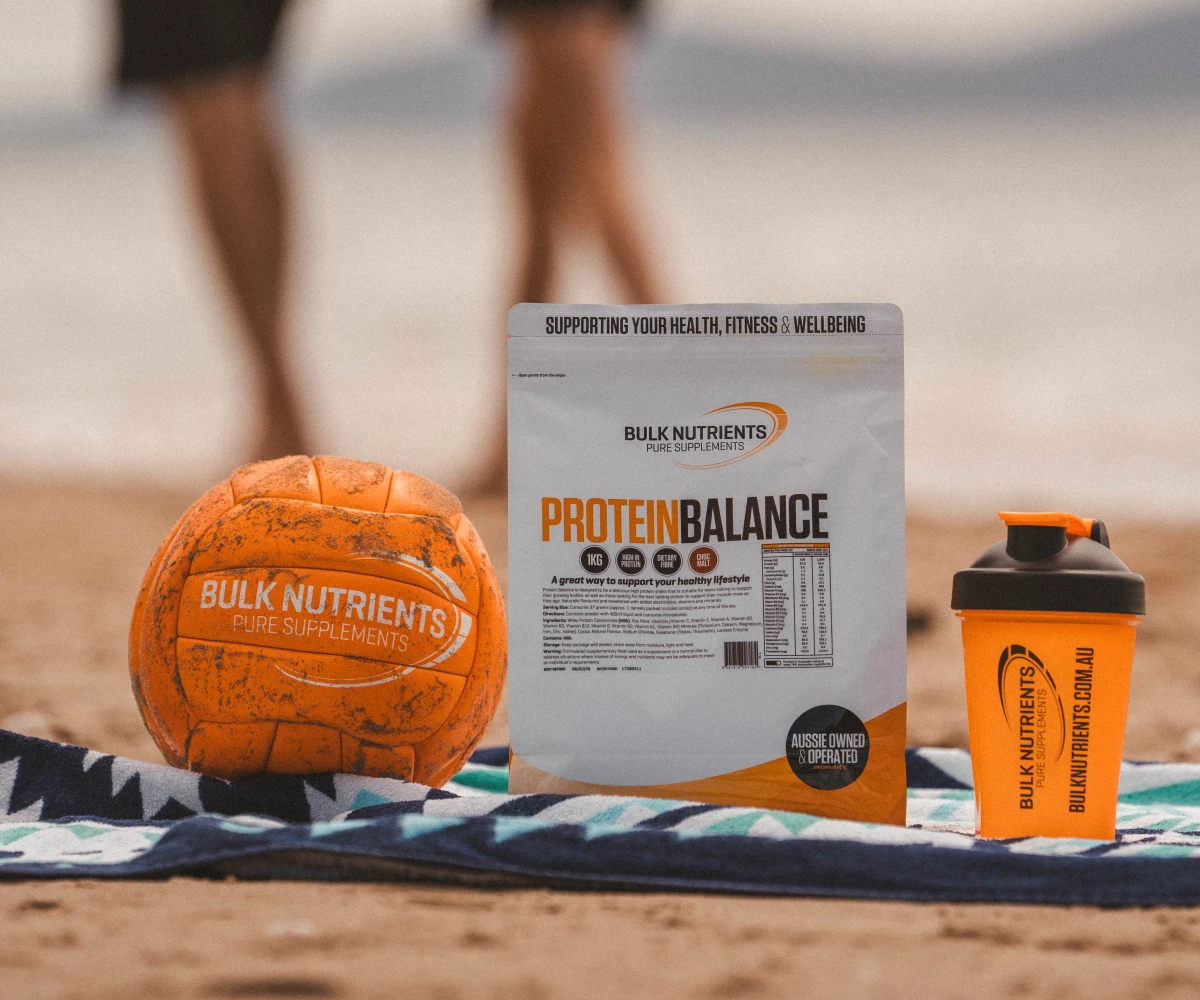 Protein Balance on a beach towel with people running past