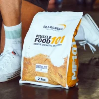 A bag of muscle food sits on the ground in front of a persons feet