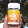 A hand holding a tub of hydration salts with palm tree behind. 