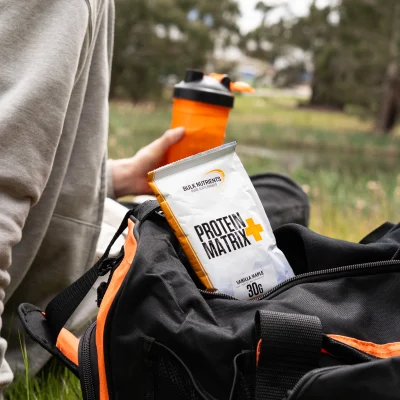A protein matrix package sits on top of a bulk nutrients bag, a bike rider rests leaning against his bike beside it.
