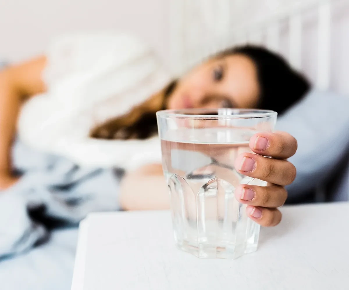 Women in bed reaching out to a glass of water