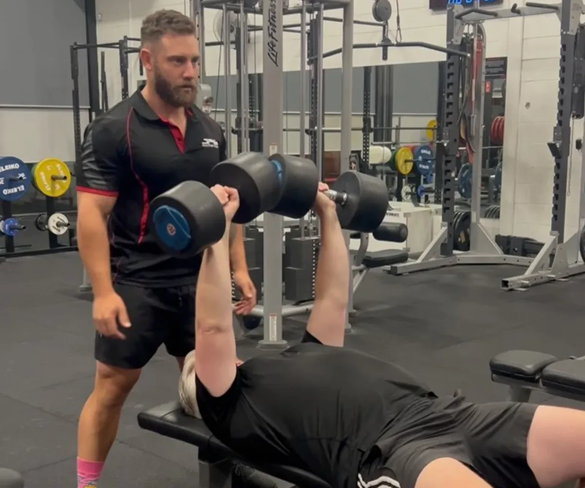 Bulk Nutrients Ambassador Sam Schepis spotting for a client in the gym