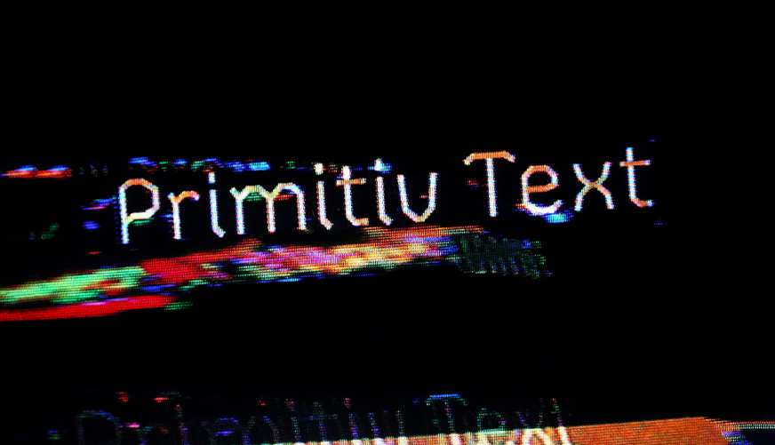 low res dark textured background from an old CRT TV with white type embedded into texture showing: Primitiv Text at an angle