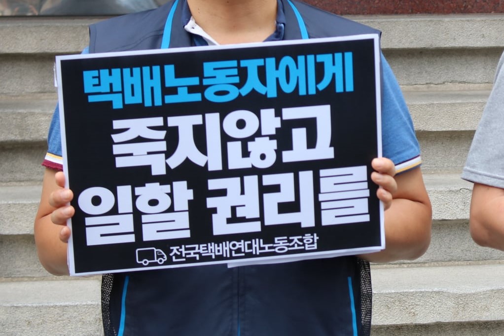 전국택배연대노동조합 소속 조합원이 '택배노동자에게 죽지 않고 일할 권리를'이라는 문구가 적힌 피켓을 들고 있는 모습
