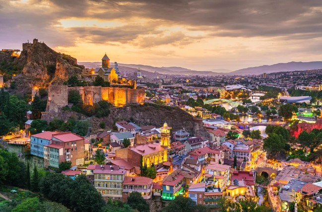 조지아 트빌리시 구시가지와 나리칼라 요새 일몰 전경, 붉은 지붕과 황금빛 석양이 어우러진 조지아 여행 명소