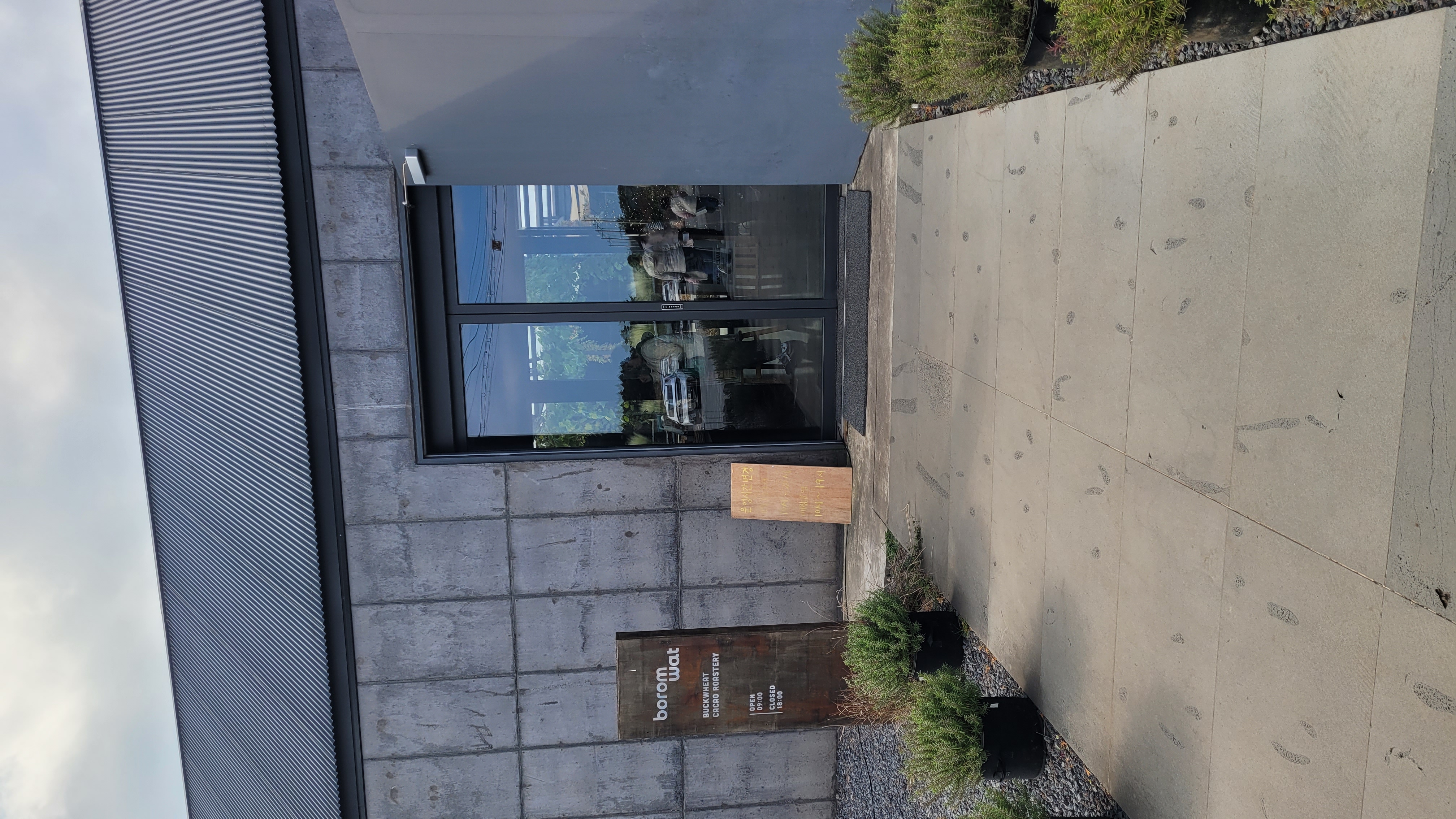 제주 서귀포 보롬왓 카페 입구 전경, 메밀과 카카오 로스터리 간판이 있는 현대적인 콘크리트 건물 외관