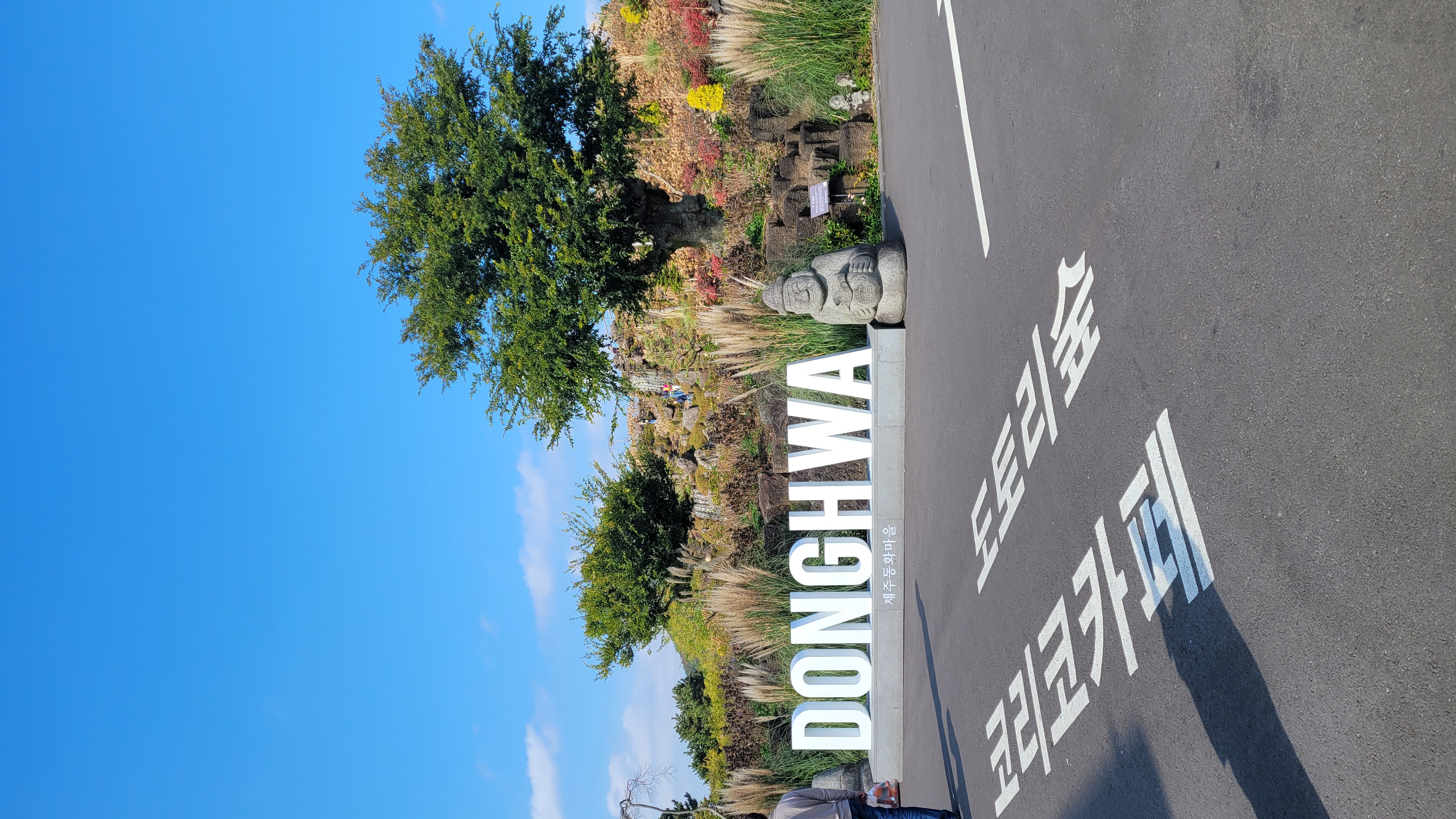 제주 동화마을 입구 포토존 - DONGHWA 대형 간판과 제주 전통 돌하르방, 600년 수령 팽나무가 보이는 메인 입구 전경
