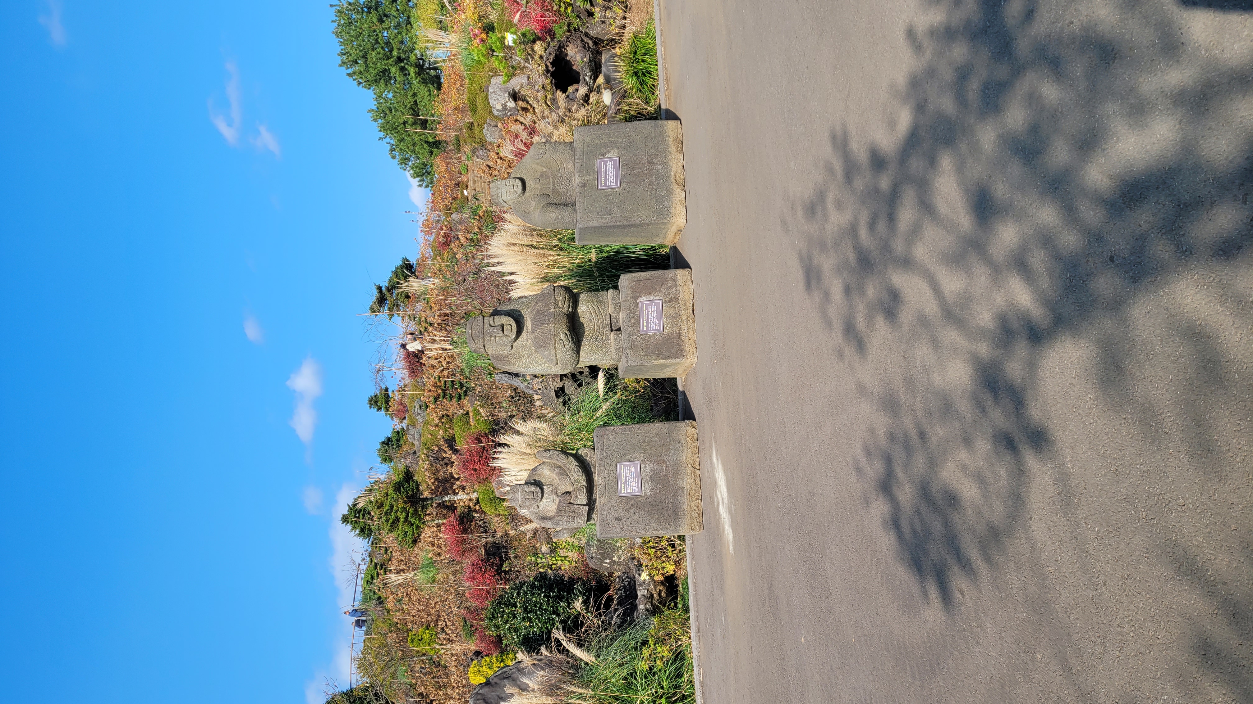 제주 동화마을 문화재급 석물 전시 - 문관석과 동자석 3점이 가을 단풍 정원을 배경으로 전시된 모습