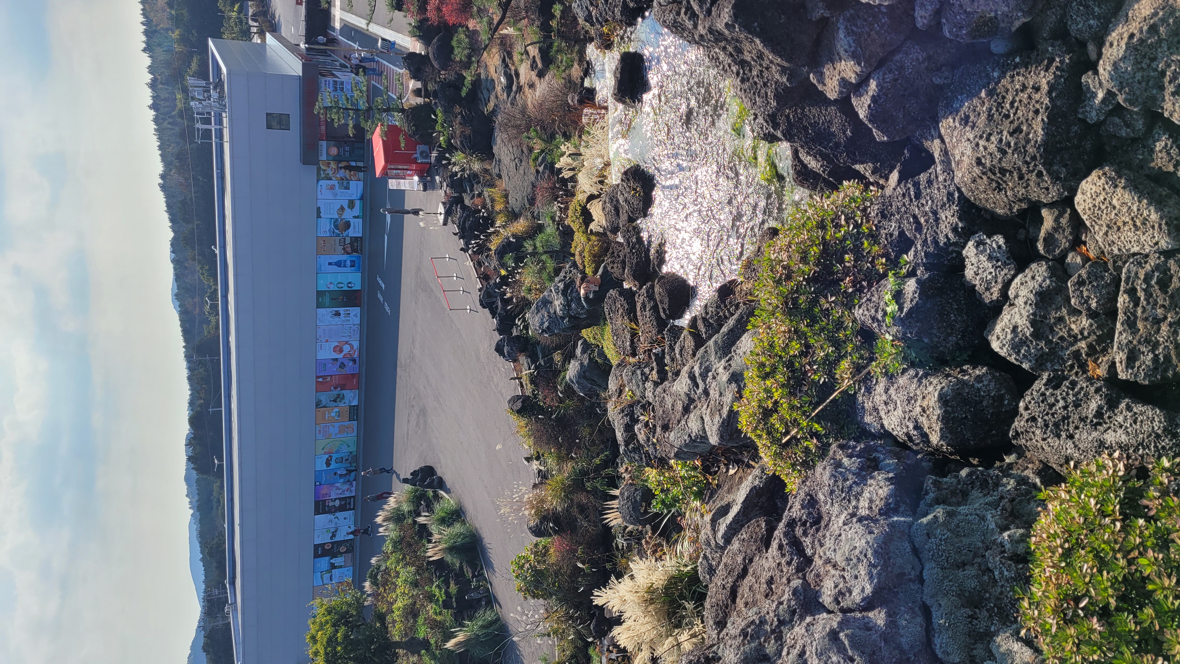 제주 동화마을 제스코관광마트 건물 전경 - 제주 특산품과 기념품을 판매하는 대형 마트와 화산석 연못이 있는 정원 조망