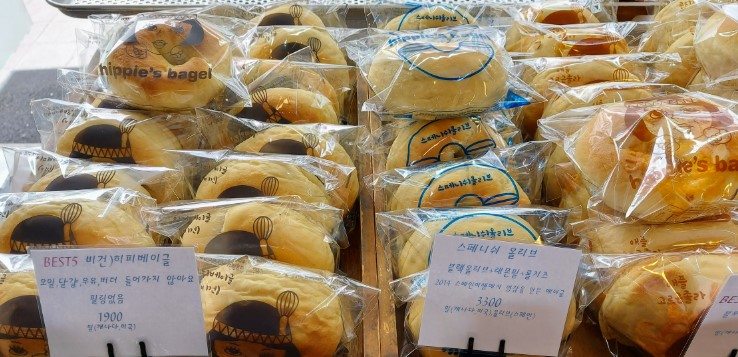 히피스베이글 매장에 진열된 다양한 종류의 수제 베이글, 개별 포장되어 있으며 가격표와 메뉴 설명이 함께 표시된 모습