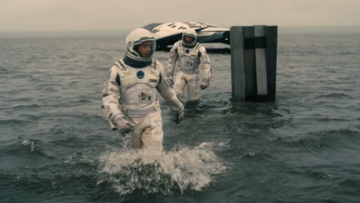 영화 인터스텔라에서 쿠퍼와 브랜드 박사가 우주복을 입고 밀러 행성의 거친 파도가 치는 바다를 헤치며 우주선으로 걸어오는 긴박한 장면