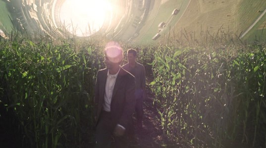 영화 인터스텔라 쿠퍼 스테이션 장면, 원통형 우주 정거장 내부 옥수수밭 사이를 걷고 있으며 뒤편에 쿠퍼가 따라오고 있고 위로 휘어진 지형과 강렬한 빛이 인상적입니다