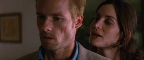 메멘토 영화 스틸컷 - 나탈리(캐리앤 모스)가 레너드(가이 피어스)에게 테디를 믿지 말라고 속삭이는 장면, 서로를 불신하게 만드는 핵심 복선