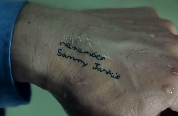 메멘토 영화 스틸컷 - 레너드 손등에 새겨진 'Remember Sammy Jankis' 문신 클로즈업, 새미가 곧 레너드 자신임을 암시하는 문신의 역설 장면