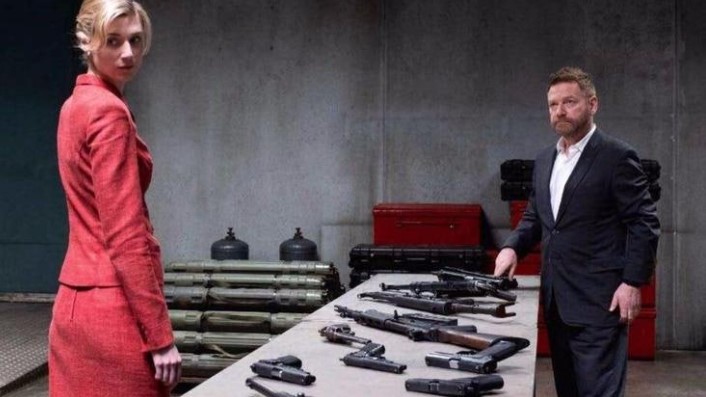 테넷 캣과 사토르 긴장 대치 장면 - 빨간 정장을 입은 캣(엘리자베스 데비키, 왼쪽)이 무기들이 가득 놓인 테이블 옆에 서 있고, 악당 사토르(케네스 브래너, 오른쪽)가 테이블에 손을 얹으며 위협적인 자세로 서 있는 장면. 말기 암으로 어차피 죽을 운명을 알고 세상 전체를 인질로 삼으려는 사토르의 집착과 공포를 보여주는 테넷의 핵심 악당 씬