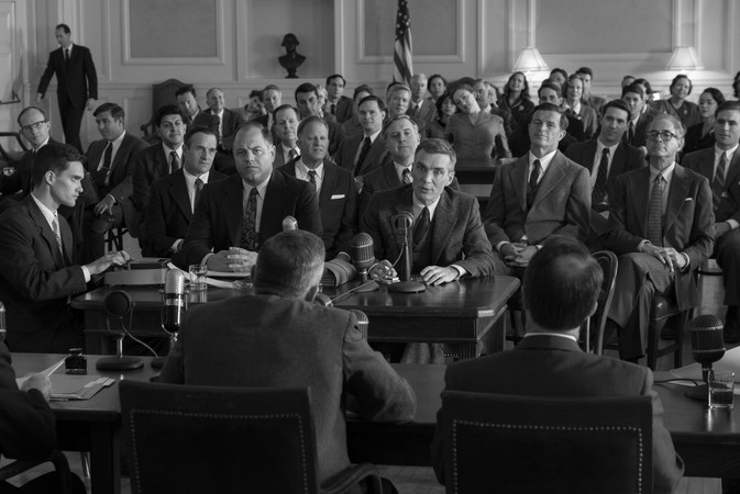 오펜하이머 결말 해석 - 1954년 보안 청문회에서 오펜하이머가 수많은 방청객이 지켜보는 가운데 마이크 앞에 앉아 증언하는 흑백 장면